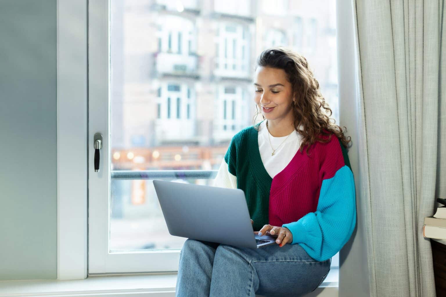 Frau sitzt am Fenster mit Laptop